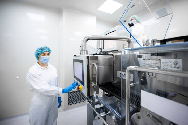 istock Woman in a protective workwear seen pushing a button on the very complex machine in a pharmaceutical laboratory 1405788661