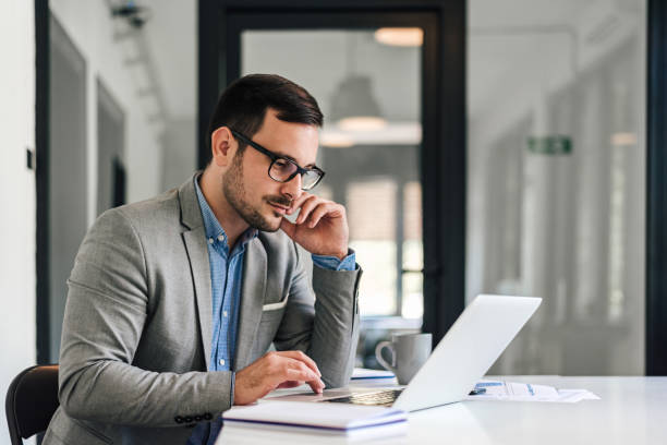 istock Serious male professional working on laptop while sitting at desk in office 1405788806