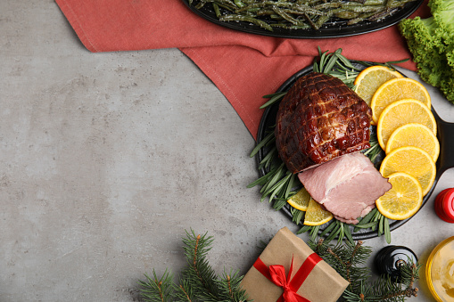 Festive flat lay composition with delicious ham on grey table, space for text. Christmas dinner