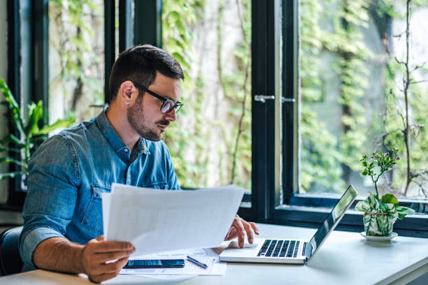 istock Serious professional holding papers while scrolling business plan on laptop 1405788848