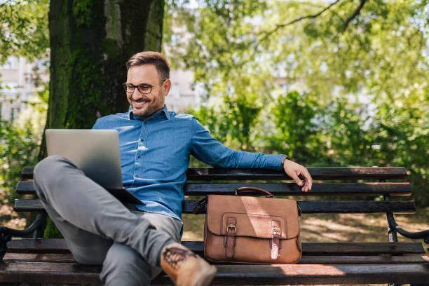 istock Confident smiling businessman analyzing plan on laptop at park bench 1405788861