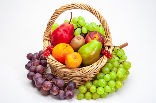 Healthy food: fresh organic fruits and vegetables in a wicker basket isolated on white background. Fruits and vegetables included in the composition are banana, grape, fig, oranges, strawberries, mango, lime, pear, apple, blue berries, kiwi, watermelon, kale, tomatoes, squash, asparagus, celery, broccoli, eggplant, onion, carrots, among others. High resolution 48,2Mp studio digital capture taken with Sony A7rII and Sony FE 90mm f2.8 macro G OSS lens