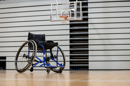 Low angle view of a empty wheelchair on a basketball sports court in the North East of England. Focus on on the wheelchair and there is a basketball hoop out of focus behind it.