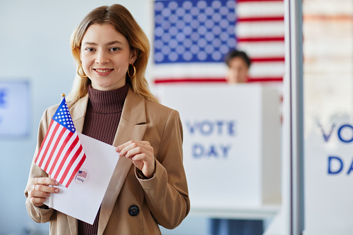People Exercising Their Civic Duty, Visiting a Modern Polling Place, Using a Ballot to Vote for an Elected Official in a Booth with the United States of America Flag. Men and Women on Elections Day
