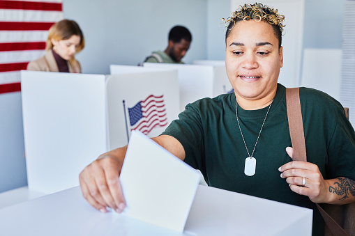 Portrait of modern American woman with tattooes voting and putting ballot in bin on election day, copy space