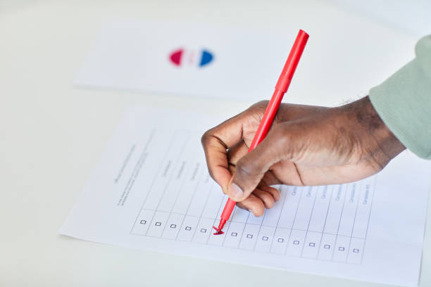 Close up of male hand ticking box in voting ballot with red pen, copy space