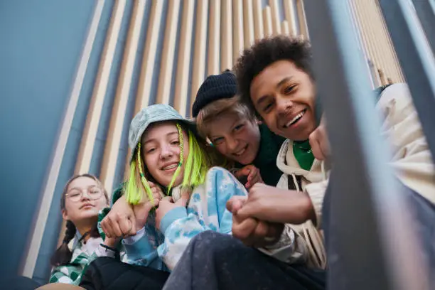 Portrait of happy close teenage friends smiling at camera while sitting on steps outdoors and embracing each other