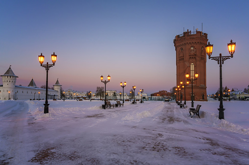 A view of the city of Tobolsk (Russia) on a cold winter evening when the street lights come on. White-stone old churches with golden domes, an old water tower, an alley and a pink-blue sky.