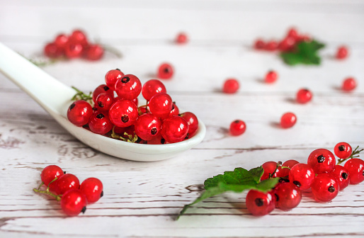 Red currant berries in white ceramic spoon on white wood background