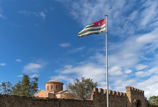 The largest flag of Abkhazia in the world overlooking the ancient Patriarchal Cathedral in Pitsunda (beginning of the 10th century) in honor of the Apostle Andrew the First-Called with a stone wall.