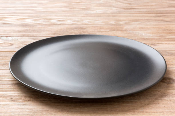 istock Perspective view of empty black plate on wooden background. Empty space for your design 1405793532