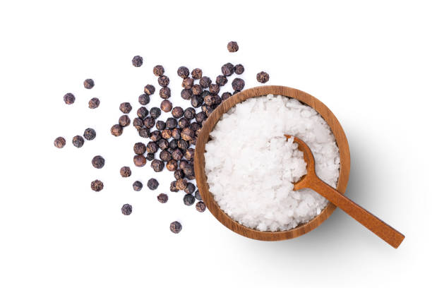 натуральная морская соль и черный перец (горошины перца), выделенные на белом фоне - spice condiment spoon wooden spoon стоковые фото и изображения