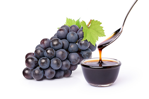 Bunch of black grape with green leaf and grape molasses in glass bowl isolated on white background.