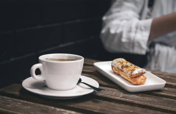 istock Cup of coffee and eclair on a wooden table close-up. 1405799208