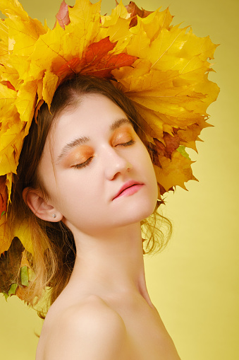 Happy autumn woman in fall leaves crown on yellow background
