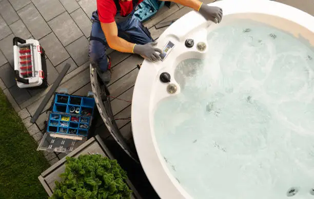 Professional Caucasian Hot Tub Technician Servicing Circular SPA Inside Residential Backyard Garden. Outdoor Bathtub Maintenance.