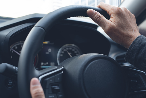 Man hands holding steering wheel, driving a car throug slight turn, close up