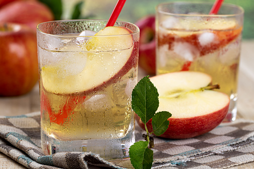 Closeup of cold glass of apple juice with sliced apples and apples in background