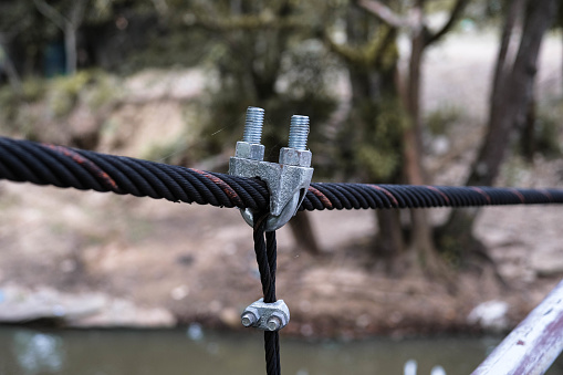 The fastening of ropes with safety locking U-Bolts made for a bridge across the river. Steel wire rope clamp for tightening sling for support suspension bridge.