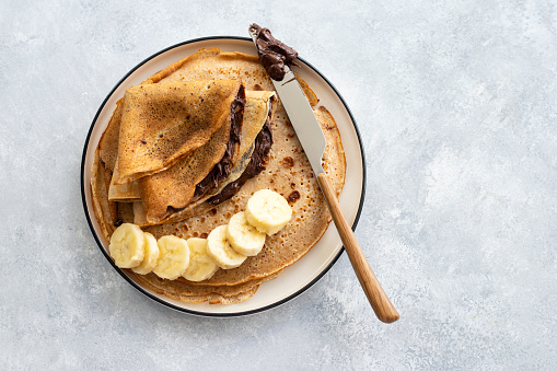 Tasty crepe with chocolate spread and banana on plate