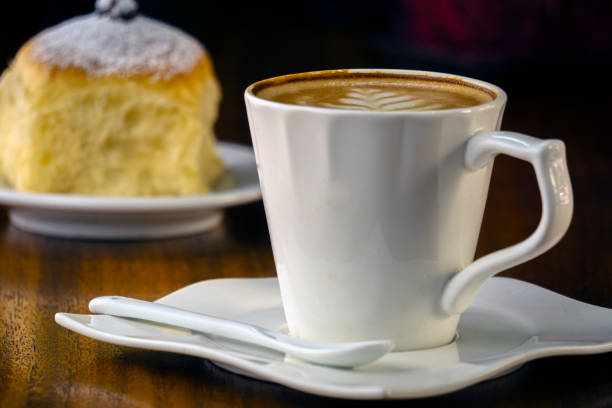 Close up of a cup with coffee and a small bread in the background. Typical snack of many Venezuelans