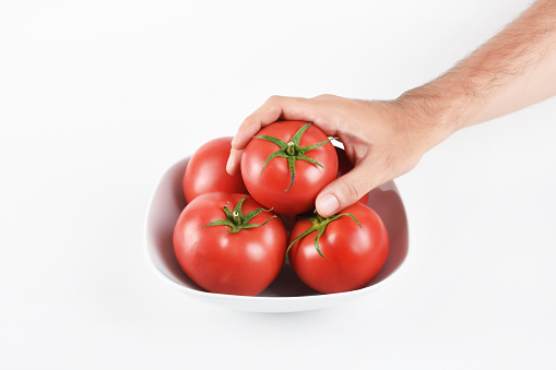Hand holding a tomato from the bowl on the white background
