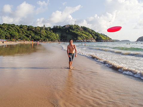 Man is playing with frisbee on Nai Harn beach on Phuket island. Leisure activity outdoors. Thailand.