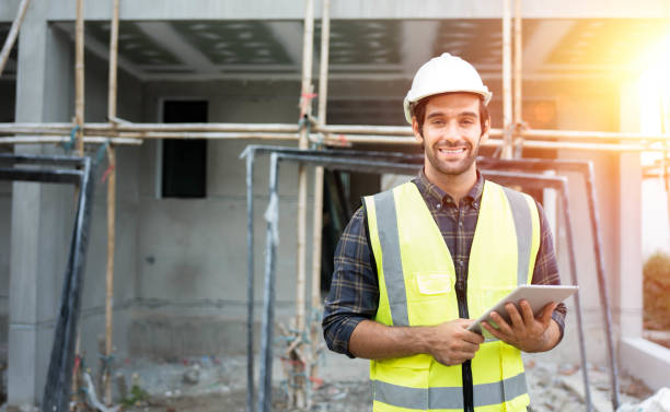 professional male civil engineer or architect wear safety helmet. engineer, inspector holding tablet technology for check list building project on construction site. look at camera with smile face. - foreman manager built structure expressing positivity imagens e fotografias de stock