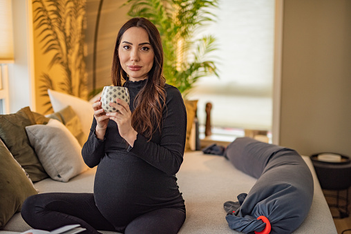 Pregnant woman holding a cup of tea while sitting on sofa in living room