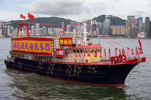 Hong Kong - June 29, 2022 : A fishing boat with banners and flags celebrating the 25th anniversary of Hong Kong's handover from Britain to China, at Victoria harbour, Hong Kong.