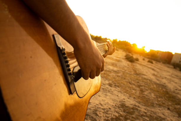 Playing an acoustic guitar during sunset. Th guitar is pointing to the sun while it is going below the horizon. The image conveys feelings of happiness and joy. guitarra y puesta de sol. tocar la guitarra acústica durante la puesta de sol. tocar música durante la puesta de sol. disfrutando de la puesta de sol con amigos y tocando música de guitarra acústica durante la hora dorada. fondos de guitarra