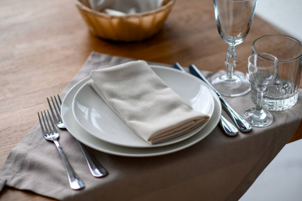 istock Festive romantic table setting with silverware, gray napkin and white crockery on beige silk tablecloth 1405831647