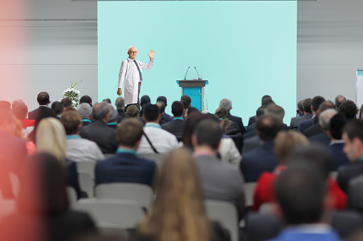Male doctor waving at audience from the stage at a medical conference event