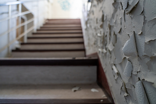 Staircase in decayed building. Focus on wall in foreground with flaking paint.