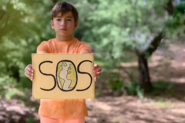 A preteen boy in a forest holds a sign that says: sos. Concept of planet care
