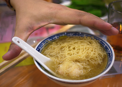 Close up High angle view a hand over the small bowl of hong kong wonton dumpling egg noodle soup, tradition local food, chinese menu