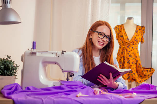 kreatywna projektantka rudowłosa kobieta w okularach, planująca nowe ubrania z kolekcji i pisząca notatki w pracowni biurowej - snow making machine zdjęcia i obrazy z banku zdjęć
