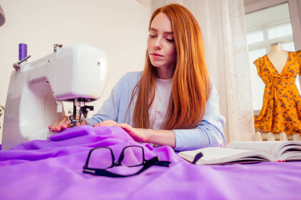 kreatywna projektantka rudowłosa kobieta w okularach, planująca nowe ubrania z kolekcji i pisząca notatki w pracowni biurowej - snow making machine zdjęcia i obrazy z banku zdjęć