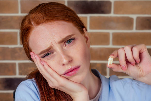redhaired ginger female with pain grimace holding white wisdom tooth after surgery removal extracted of a tooth stock photo