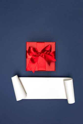 Red gift box with red ribbon on navy blue background and white empty card.