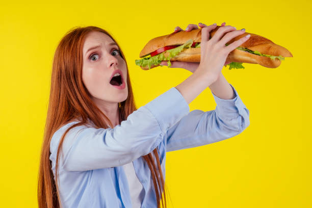 beautiful redhaired ginger woman real jam licking fingers holding huge sandwich Titanic in studio yellow background beautiful redhaired ginger woman real jam licking fingers holding huge sandwich Titanic in studio yellow background. big fat lips stock pictures, royalty-free photos & images