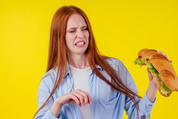 istock disgust distaste aversion redhaired ginger woman holding huge sandwich with pepper and lettuce salad between bun in studio yellow background 1405840544