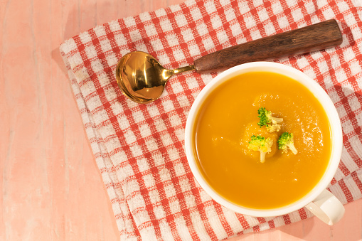 Butternut squash and carrot soup in blow on orange background close up, top view, healthy food concept.