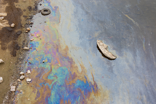 Industrial debris and colored stains of gasoline or oil on the water surface near the river bank. Concept ecological problems and environmental pollution.