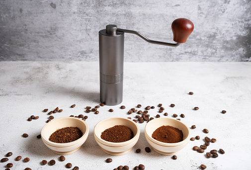 Different degrees of grinding of natural coffee next to a manual coffee grinder. Horizontal orientation