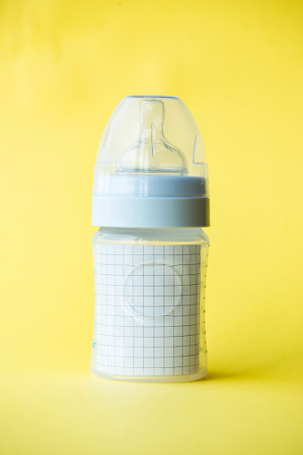 Checkered paper in feeding bottle on yellow background. Representing expenses , trending consumerism and overall issues of a new born.