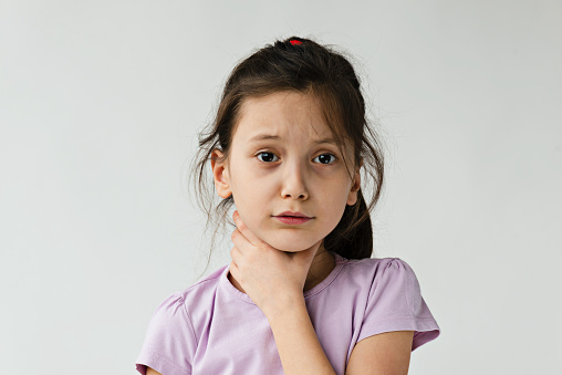Little girl is holding her throat in pain in front of white background.