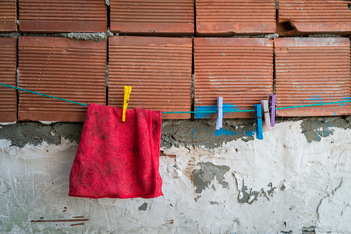 Colorful clothespins and dirty red cloth standing on a stretched clothesline in front of red brick and plaster.