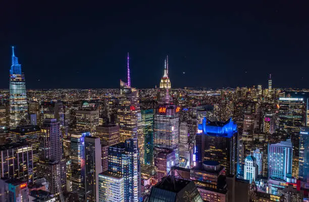 Photo of Night city scene of tall downtown skyscrapers in metropolis. High rise buildings with colour illuminated spires on tops. Manhattan, New York City, USA