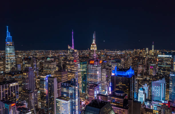 ночная городская сцена высоких небоскребов в центре города в мегаполисе. высотные здания с цветными шпилями на вершинах. манхэттен, нью-йор - new york city new york state manhattan night стоковые фото и изображения